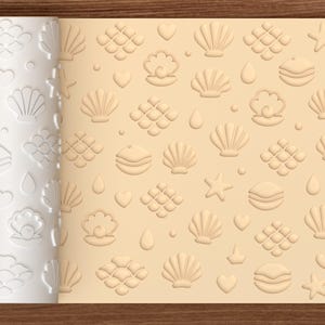 May include: A white cylindrical rolling pin with a raised pattern of seashells, starfish, hearts, and scales, shown next to a light tan sheet of dough embossed with the same repeating nautical motifs. The text Crave is visible in the bottom corner.
