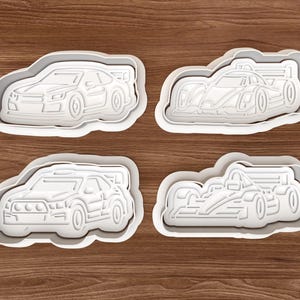 Könnte beinhalten: Vier weiße Ausstecher aus Kunststoff in Form von Rennwagen. Die Ausstecher umfassen einen Sportwagen, einen Rennwagen, einen Rallye-Wagen und einen Formel-1-Wagen. Auf einer Holzoberfläche.