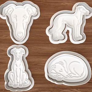 Puede incluir: Un juego de cuatro cortadores de galletas de plástico blanco con forma de galgos en varias posturas: un retrato de cabeza, uno de pie, uno sentado y uno durmiendo enroscado. Cada cortador presenta un borde elevado y detalles internos.