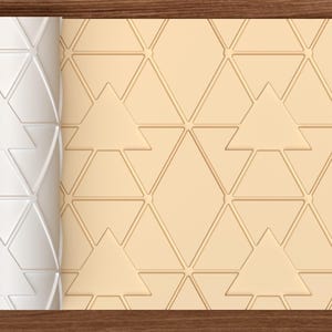 Op de afbeelding: Een witte cilindrische deegroller met een verhoogd geometrisch patroon van driehoeken en ruiten, naast een plat, lichtbeige oppervlak dat is voorzien van hetzelfde herhalende driehoeks- en ruitenpatroon over het gehele oppervlak.