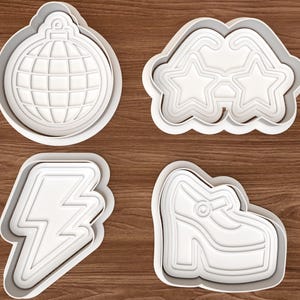 May include: A set of four white plastic cookie cutters featuring a disco ball, star-shaped glasses, a lightning bolt, and a platform shoe. Each cutter has a defined outline and internal impression detail for creating shaped cookies with distinct designs.