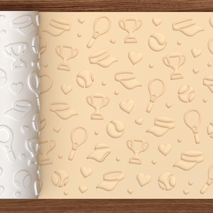 May include: A cylindrical white rolling pin featuring a repeating embossed pattern of tennis rackets, tennis balls, trophies, visors, and hearts. The pattern is shown imprinted on a flat, light beige surface, displaying the design clearly.
