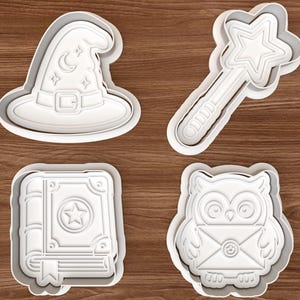 Pode incluir: Quatro cortadores de biscoitos de plástico branco com um tema fantasioso. As formas incluem um chapéu de mago com uma lua e estrelas, uma varinha com uma estrela, um livro com uma estrela e uma coruja segurando um envelope. Os cortadores estão em uma superfície de madeira.