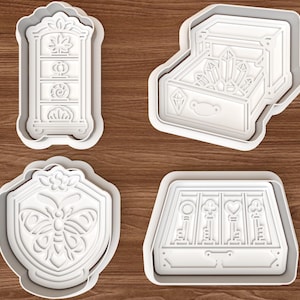 May include: Four white plastic cookie cutters featuring detailed designs: a tall cabinet with shelves, an open chest filled with crystals, a shield-shaped frame with a butterfly, and a rectangular box containing four keys with different head shapes.