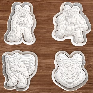 May include: Four white plastic cookie cutters featuring detailed embossed designs of horned, fur-covered creatures. Each cutter depicts a different pose of the figure, including one holding a bundle of sticks, one with bells, one carrying a basket, and a portrait.