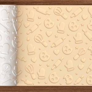 May include: A white cylindrical rolling pin with an embossed pattern of baking tools including whisks, rolling pins, oven mitts, cookies, and hearts, shown next to a light tan dough sheet featuring the same imprinted baking-themed design.