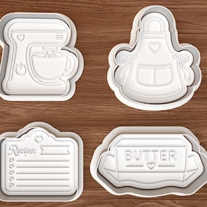 May include: Four white plastic cookie cutters in the shapes of a stand mixer, apron, recipe card, and butter container. The recipe card has the word "Recipe" and a list. The butter container has the word "BUTTER".
