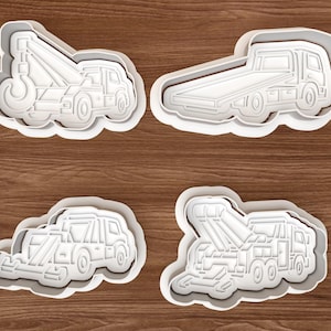 Puede incluir: Un juego de cuatro cortadores de galletas de plástico blanco con formas de diversos camiones de remolque y vehículos de plataforma. Cada cortador presenta contornos detallados de las cabinas, ruedas y mecanismos de elevación de los camiones.