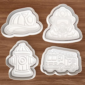 Peut inclure: Quatre emporte-pièces blancs en forme de casque de pompier, de pompier avec masque, de borne-fontaine et de camion de pompiers. Les emporte-pièces sont sur une surface en bois.