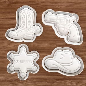 May include: Four white plastic cookie cutters in a Western theme. The shapes include a cowboy boot, a revolver, a sheriff's badge with the word "SHERIFF", and a cowboy hat. The cutters are on a wooden surface.