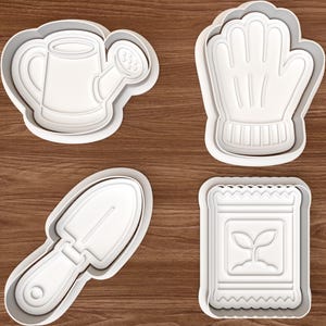 Könnte beinhalten: Vier weiße Ausstecher aus Kunststoff in Form von Gartengeräten. Das Set enthält eine Gießkanne, einen Gartenhandschuh, eine Kelle und eine Saatguttüte. Die Ausstecher befinden sich auf einer braunen Holzoberfläche.