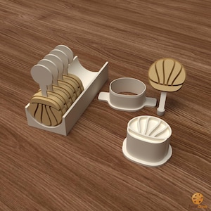 May include: A set of white plastic cookie cutters and stamps featuring a shell design. The collection includes a rectangular storage tray holding several stamps, a circular cutter, and a single shell-shaped stamp with a tan top.