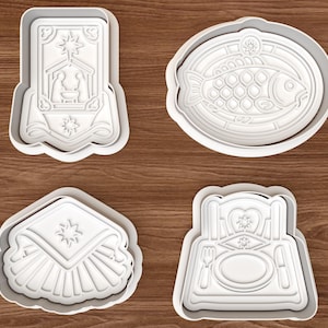 May include: Four white plastic cookie cutters featuring detailed embossed designs: a nativity scene, a fish on a platter, a folded napkin with a star, and a formal place setting with a plate, fork, and knife. Each cutter has a raised border.