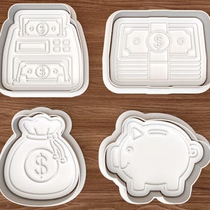 May include: Four white plastic cookie cutters in the shapes of money-related items. The shapes include a cash register, a stack of bills, a money bag, and a piggy bank. The cutters are on a wooden surface.