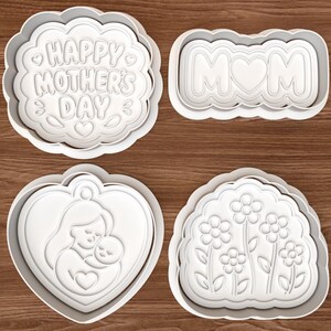 May include: Four white plastic cookie cutters with scalloped edges. One says "HAPPY MOTHER'S DAY", another says "MOM" with a heart, a third shows a mother and child, and the last has flowers.
