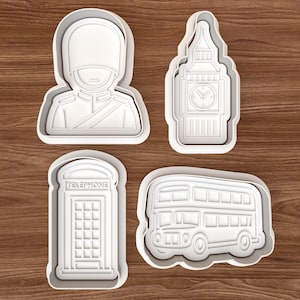 May include: Four white plastic cookie cutters in the shapes of a British Royal Guard, Big Ben clock tower, a red telephone booth, and a double-decker bus. The cutters are on a wooden surface.