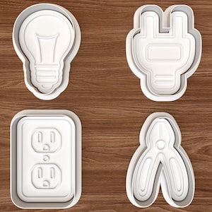 May include: A set of four white plastic cookie cutters featuring electrical-themed shapes: a light bulb, an electrical plug, a dual wall socket, and a pair of pliers. Each cutter has a raised edge for cutting and an inner embossed detail.