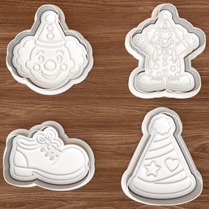 Puede incluir: Cuatro cortadores de galletas de plástico blanco con forma de cara de payaso, figura completa de payaso, zapato de payaso y gorro de fiesta con diseños de estrella y corazón. Sobre una superficie de madera marrón.