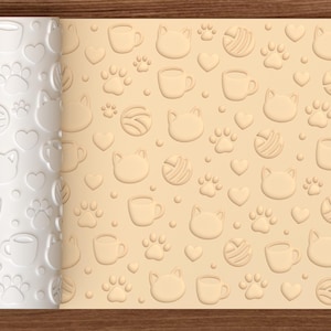 May include: A white cylindrical rolling pin with a repeating embossed pattern of cat faces, paw prints, yarn balls, hearts, and coffee mugs. The rolling pin is shown next to a light tan surface displaying the same pattern pressed into the material.