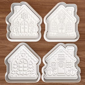 May include: Four white plastic gingerbread house cookie cutters with detailed designs. Each cutter features a different house design, including snowflakes, wreaths, and snowmen. Perfect for holiday baking.