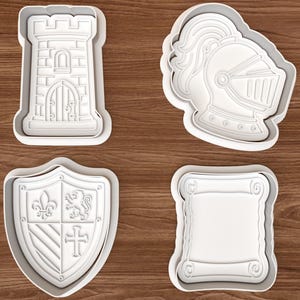 Puede incluir: Cuatro cortadores de galletas de plástico blanco con temática medieval. Las formas incluyen una torre de castillo, un casco de caballero, un escudo con símbolos heráldicos y un pergamino. Los cortadores están sobre una superficie de madera.