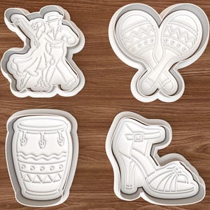 May include: Four white plastic cookie cutters in the shapes of a dancing couple, maracas, a conga drum, and a high-heeled sandal. The cutters are on a brown wooden surface.