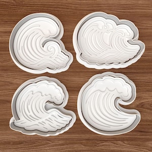 Puede incluir: Cuatro cortadores de galletas blancos de plástico con forma de ola y patrones detallados. Los cortadores están dispuestos sobre una superficie de madera, ideales para crear dulces con temática oceánica. El diseño incluye una parte superior redondeada y una base curva.
