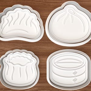 Könnte beinhalten: Ein Set aus vier weißen Kunststoff-Ausstechformen mit Motiven eines gefalteten Dumplings, eines runden Bao-Brötchens, eines gerüschten Shumai und eines gestapelten Bambusdampfkorbs, jeweils mit erhöhtem Rand und detaillierten Prägungen.