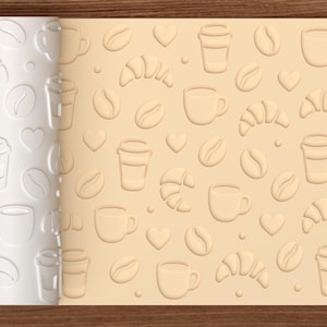 May include: A white cylindrical rolling pin featuring a repeating embossed pattern of coffee beans, coffee cups, croissants, and hearts. The rolling pin is shown next to a light tan sheet of dough that displays the same imprinted design.