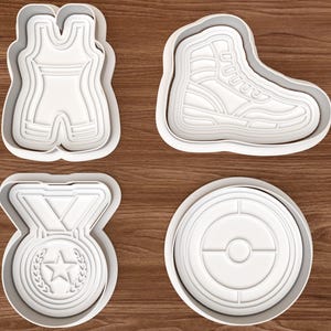 May include: A set of four white plastic cookie cutters featuring a wrestling singlet, a high-top athletic shoe, a circular medal with a star and laurel wreath design, and a circular target-like emblem with a central dot and segmented lines.