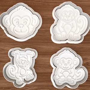 Può includere: Un set di quattro stampini per biscotti in plastica bianca con disegni di scimmie. La collezione include una faccia di scimmia, due scimmie sedute e una scimmia appesa a una barra orizzontale, tutte con dettagli in rilievo su viso e corpo.