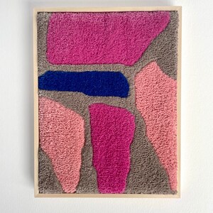 May include: A framed abstract wall art piece with a textured, fuzzy surface. The artwork features a variety of shapes in shades of pink, gray, and blue.