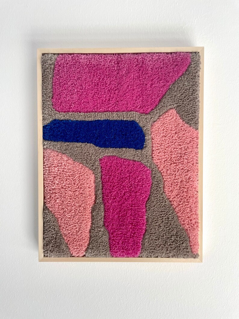 May include: A framed abstract wall art piece with a textured, fuzzy surface. The artwork features a variety of shapes in shades of pink, gray, and blue.
