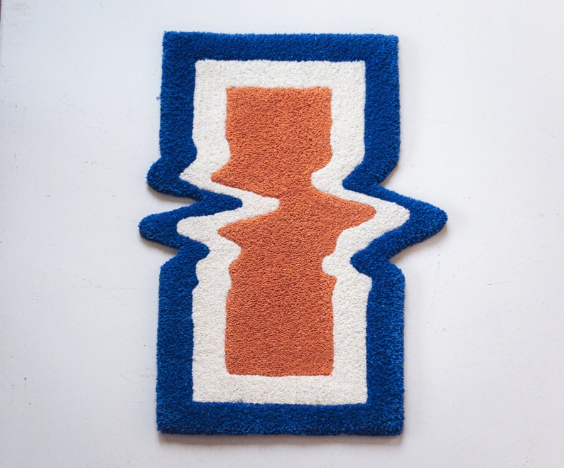 Puede incluir: Una alfombra azul, blanca y naranja con un dise&ntilde;o abstracto ondulado. La alfombra tiene una pila gruesa y texturizada.