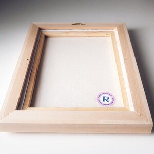 May include: A wooden frame with a white canvas inside. The frame has a pink sticker with the letters "R" and "R" in blue.