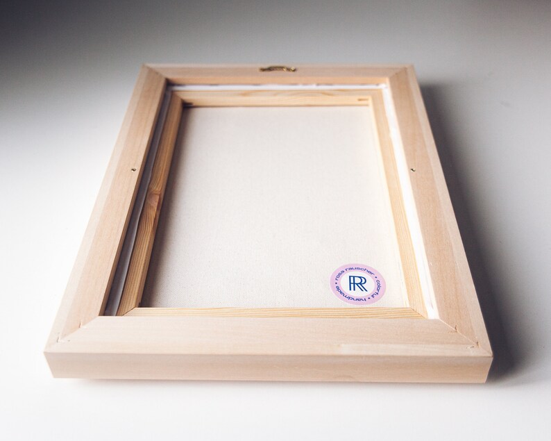 May include: A wooden frame with a white canvas inside. The frame has a pink sticker with the letters "R" and "R" in blue.