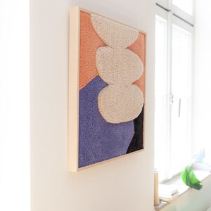 May include: A framed abstract wall art piece with a textured, fluffy design in shades of peach, white, purple, and black.