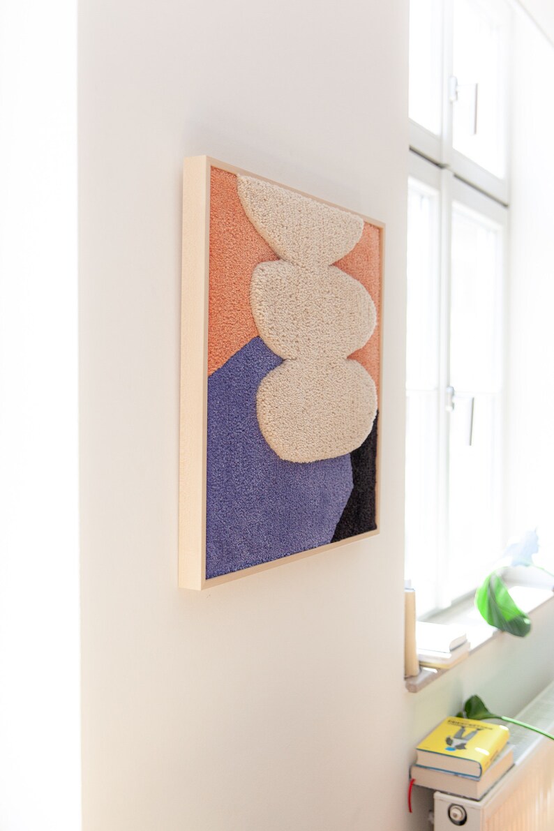 May include: A framed abstract wall art piece with a textured, fluffy design in shades of peach, white, purple, and black.