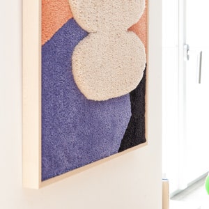 May include: A framed abstract wall art piece with a textured, fuzzy surface. The artwork features a combination of peach, purple, black, and white colors.