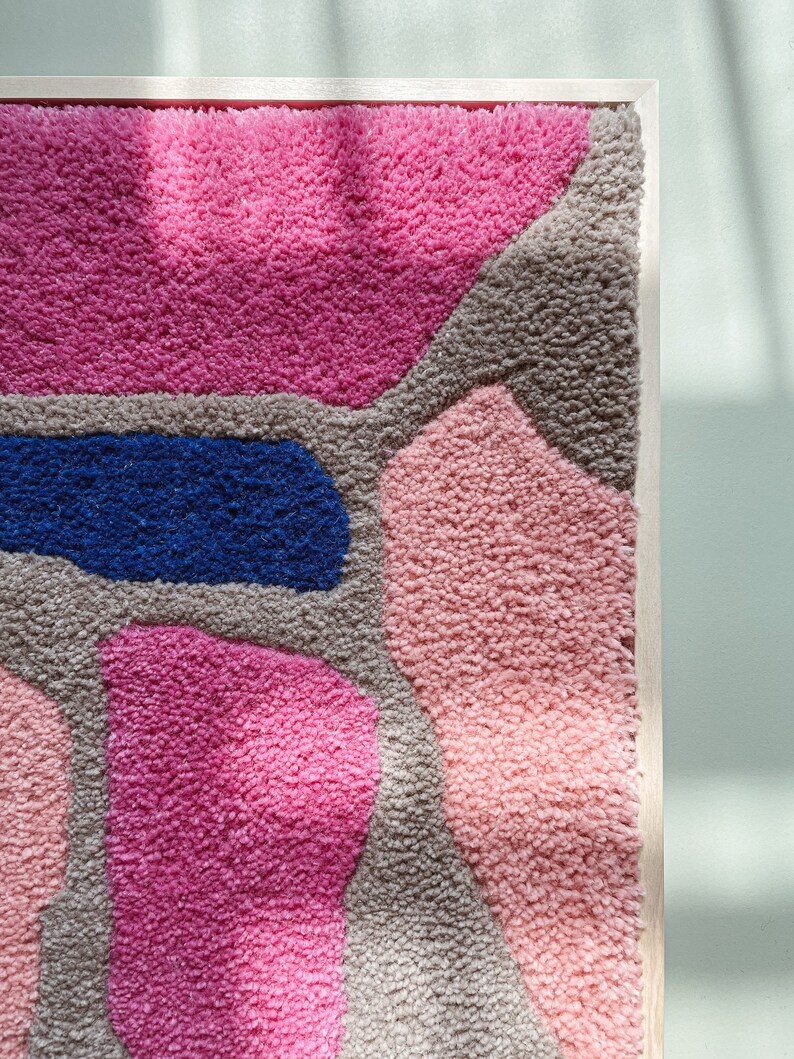 May include: A framed wall hanging with a colorful abstract design. The design features various shapes and colors, including pink, blue, and brown. The shapes are made of a fluffy, textured material.