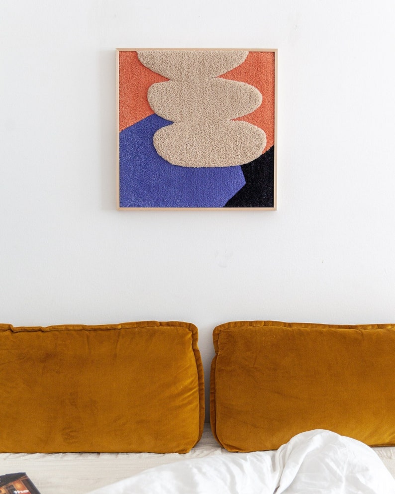 May include: A framed abstract wall art piece with a textured, beige, oval shape on a background of orange, blue, and black.