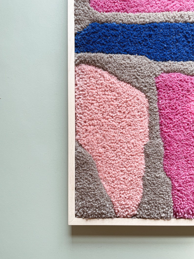 May include: A framed abstract wall art piece with a textured, fuzzy surface. The artwork features a variety of shapes and colors, including pink, blue, and gray.