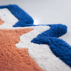 Puede incluir: Primer plano de una alfombra colorida con un patr&oacute;n ondulado en tonos naranja, blanco y azul.