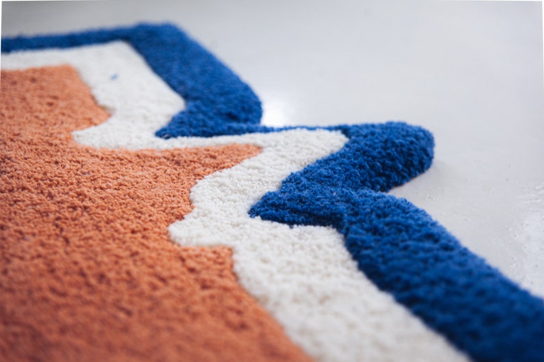 Puede incluir: Primer plano de una alfombra colorida con un patr&oacute;n ondulado en tonos naranja, blanco y azul.