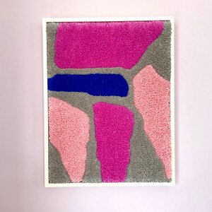 May include: A framed abstract wall art piece with a gray background and pink and blue shapes. The shapes are made of fluffy yarn.