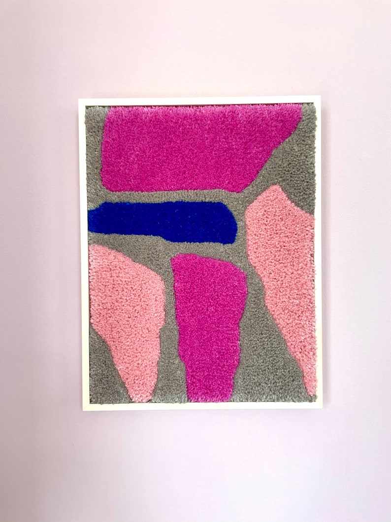 May include: A framed abstract wall art piece with a gray background and pink and blue shapes. The shapes are made of fluffy yarn.