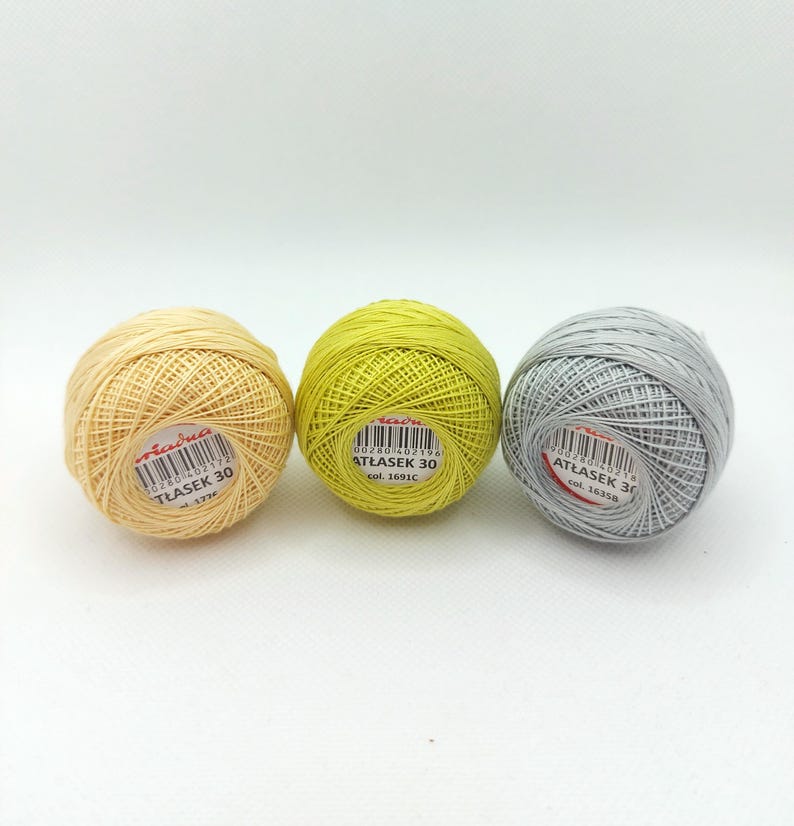 May include: Three balls of embroidery floss in yellow, green, and gray. Each ball has a label with the text "ATŁASEK 30" and a color code.