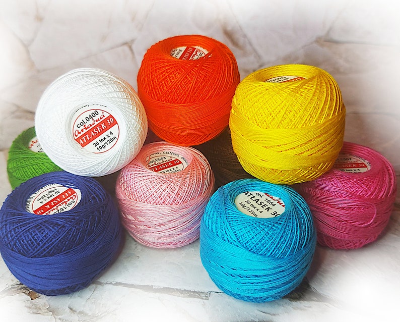May include: Assortment of colorful yarn balls, each with a label indicating the brand "Arraduci" and "Atlaser 30". The yarn balls are in shades of white, orange, yellow, pink, blue, and green.