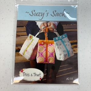 May include: A sewing pattern for a small bag called "Suzy's Sack" by This & That. The pattern is #238 and shows three different bags in bright colors with floral and geometric patterns.