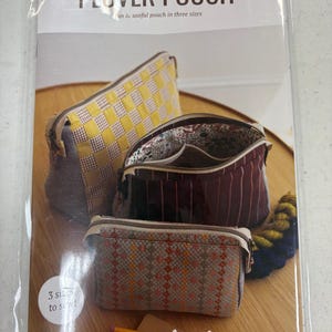 May include: A sewing pattern for a Plover Pouch in three sizes. The pattern includes instructions for sewing a yellow and white checkered pouch, a burgundy striped pouch, and a beige and orange patterned pouch. The pattern is from Noodlehead.